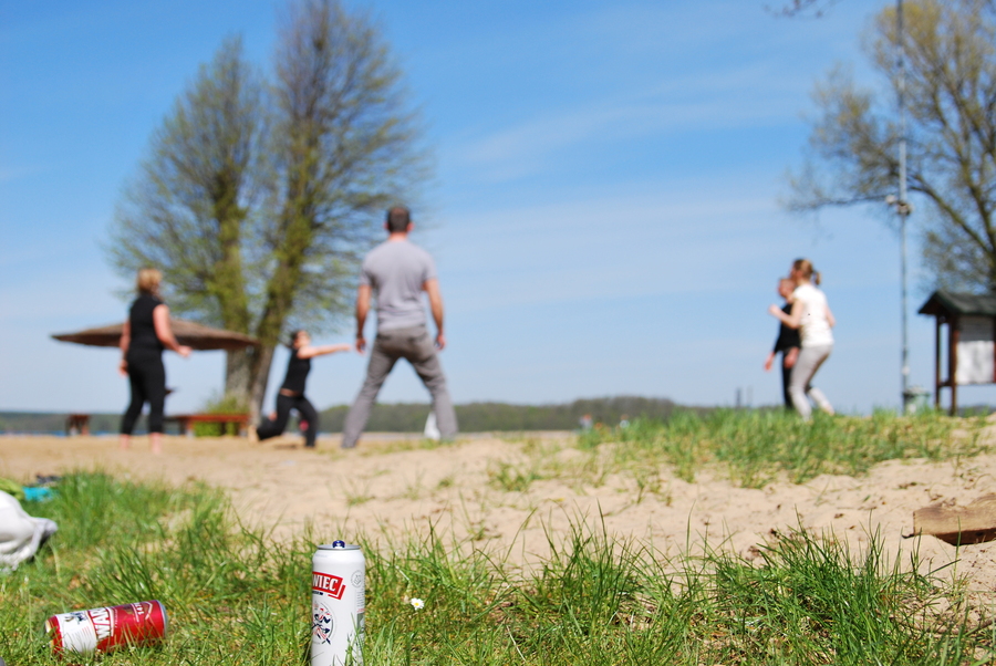 A picture of people playing volleyball with 2 cans of beer in the foreground
